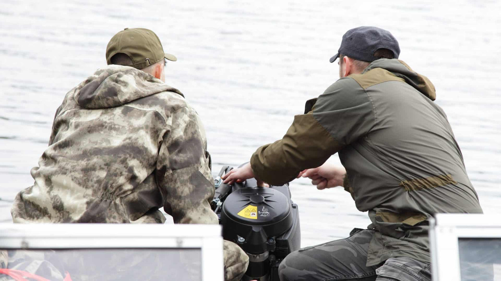 Two men on a small boat trying to fix an outboard engine